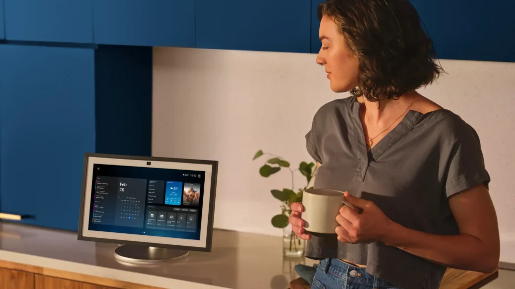 Woman using Alexa+ smart display in a modern kitchen while holding a mug